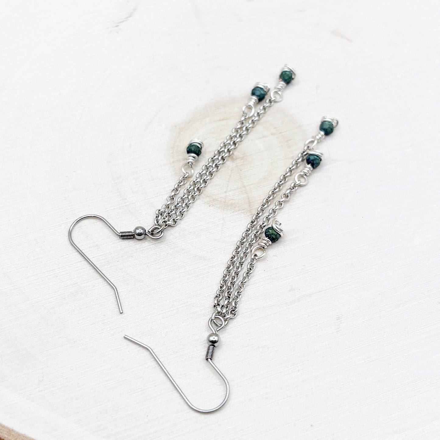Silver chain earrings with green beads on a white background