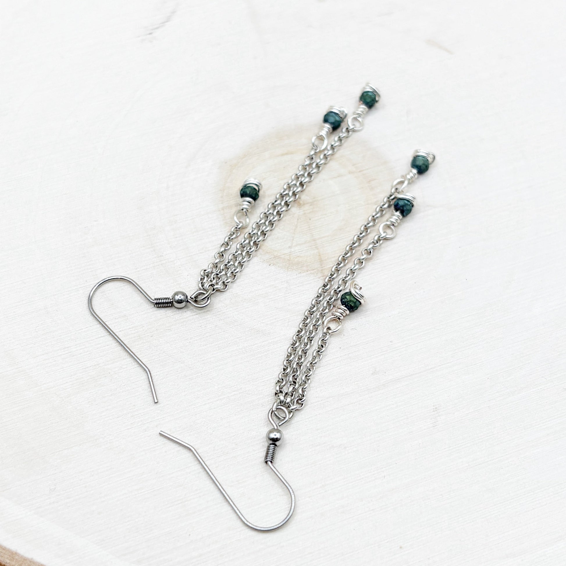 Silver chain earrings with green beads on a white background