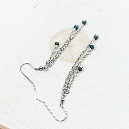 Silver chain earrings with green beads on a white background
