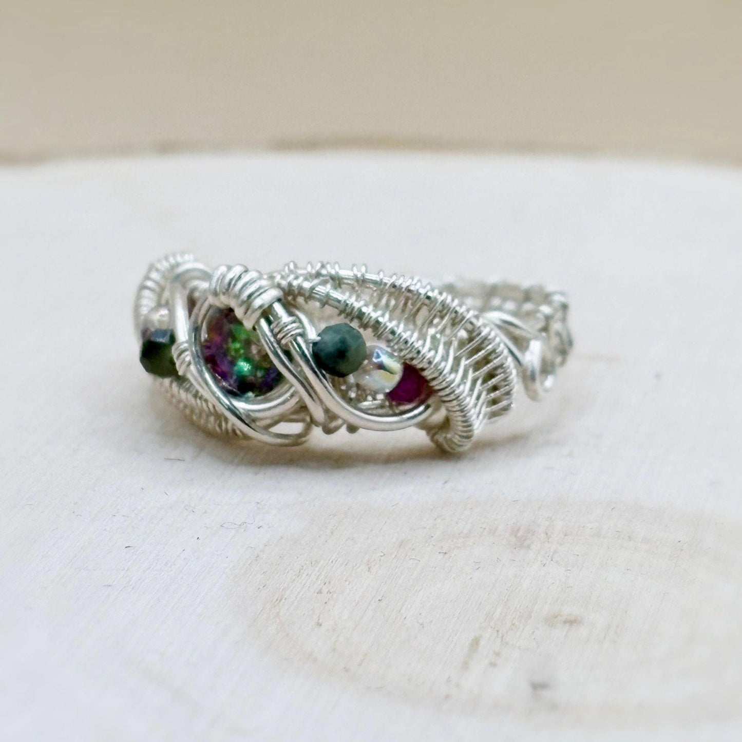 Silver wire-wrapped ring with colorful gemstones on a white surface