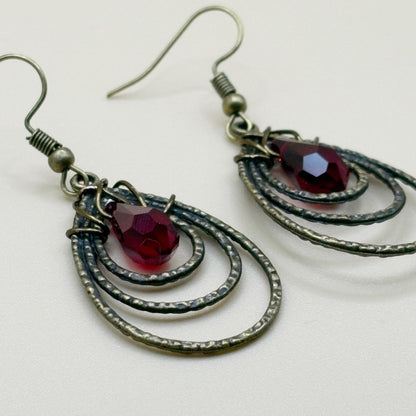 Pair of earrings with red gemstones and metallic loops on a white background
