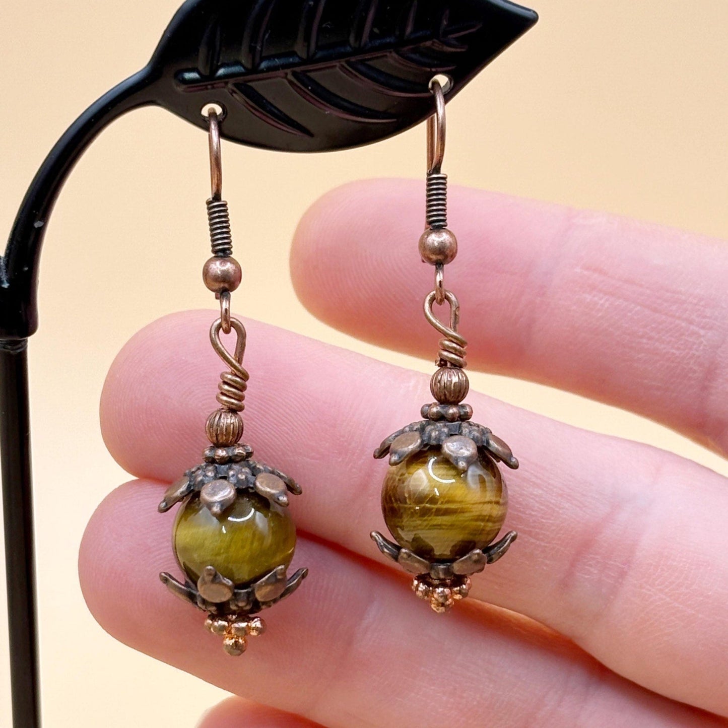 Pair of copper and brown beaded earrings held between fingers against a beige background