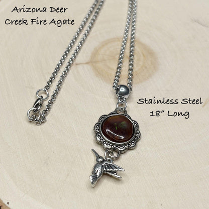 Silver necklace with a fire agate stone and hummingbird charm on a beige background