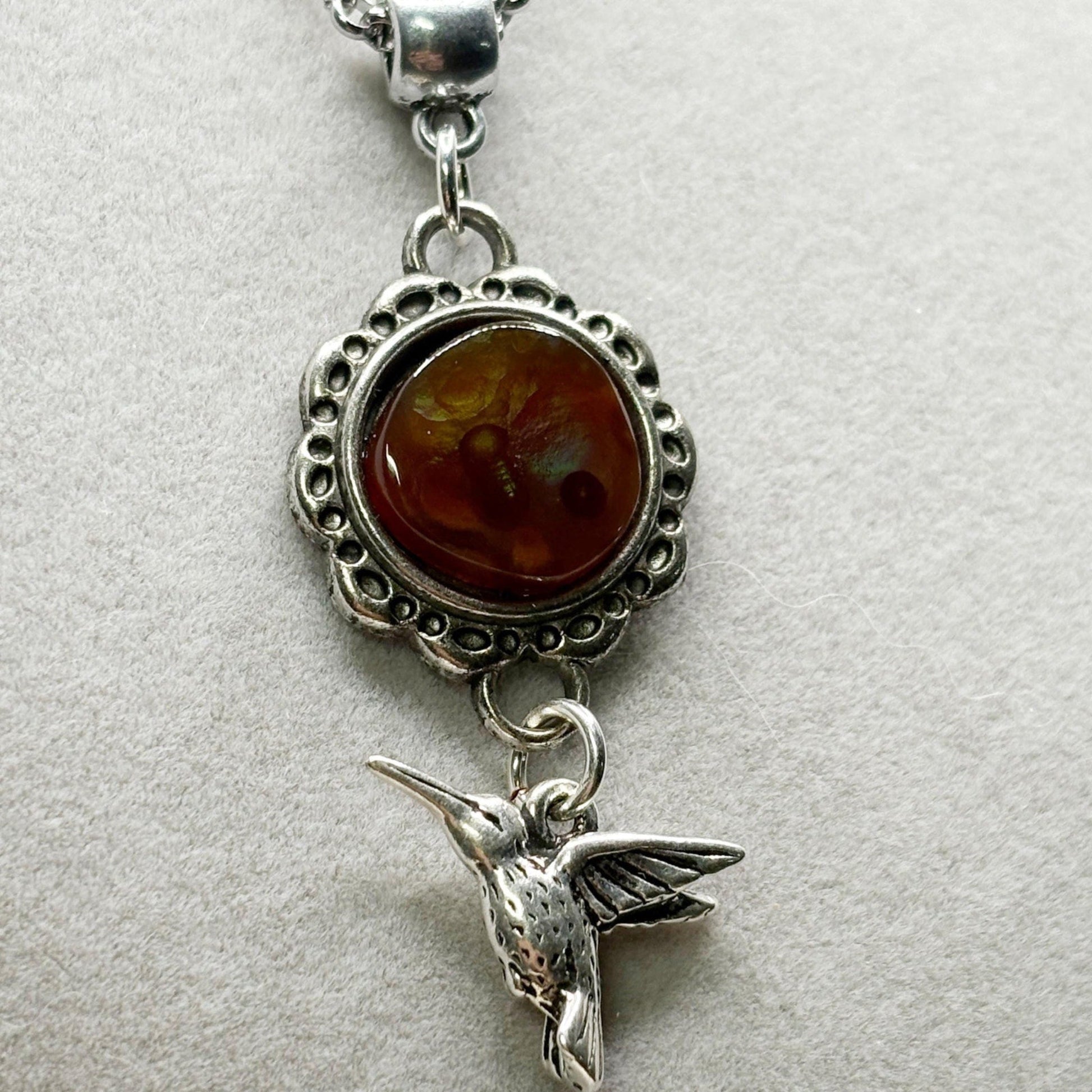 Silver pendant with agate stone and hummingbird charm on a light gray background