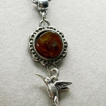 Silver pendant with agate stone and hummingbird charm on a light gray background