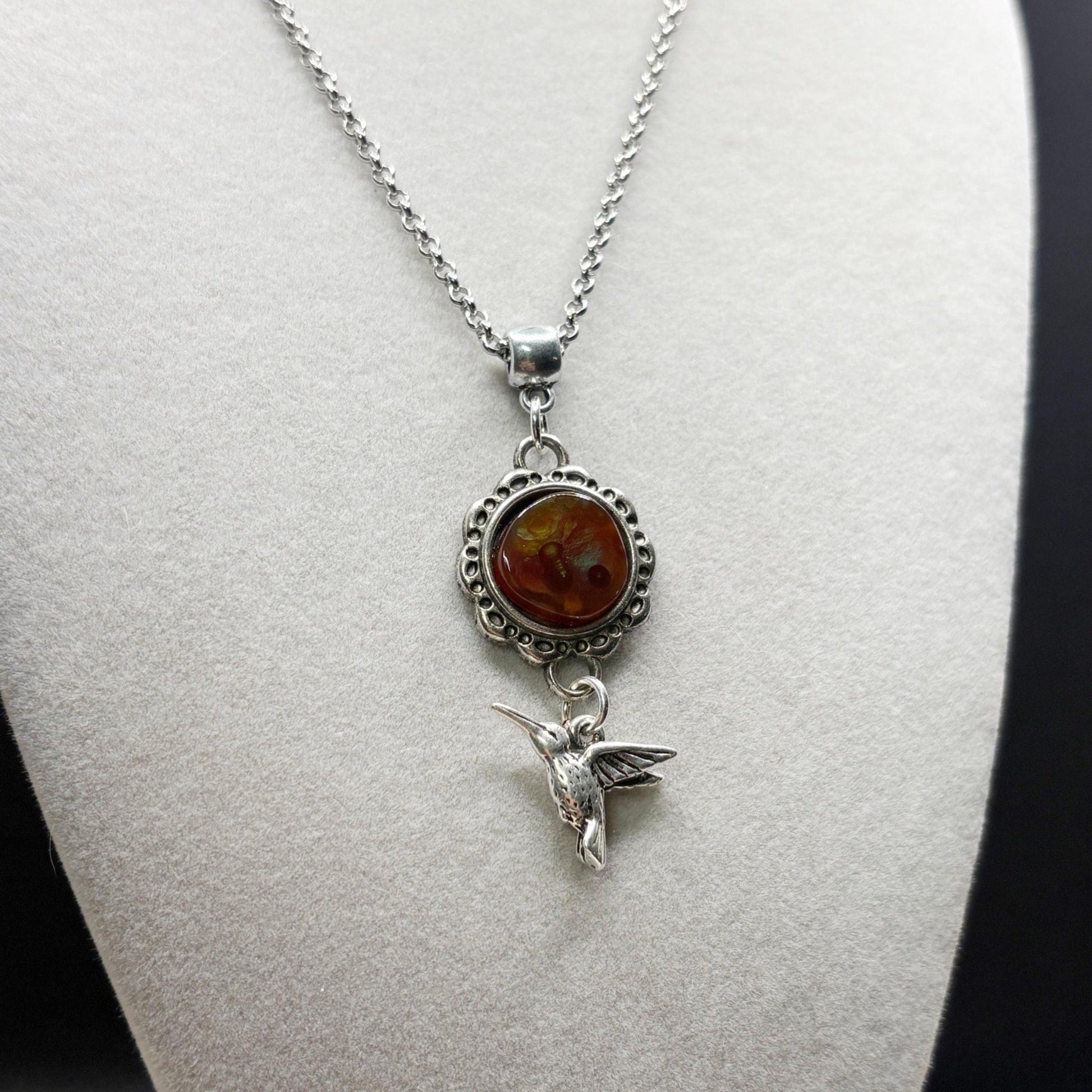 Silver necklace with fire agate pendant and hummingbird charm on a mannequin bust.