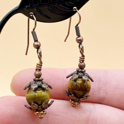 Pair of earrings with tiger eye stones held between fingers against a beige background