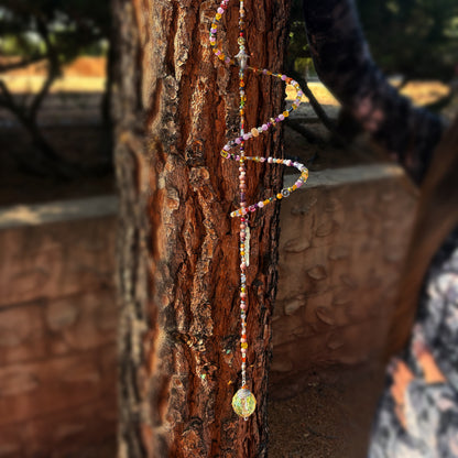 Colorful beaded sun catcher hanging on a tree trunk with a blurred background