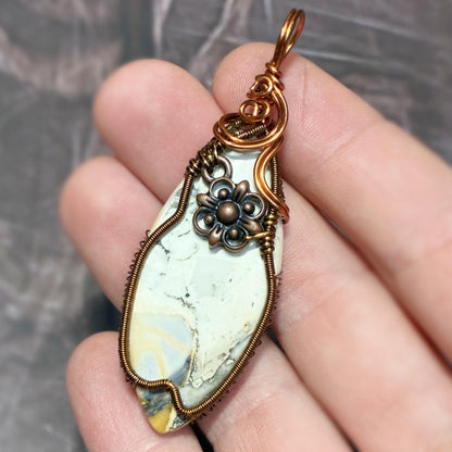hand holding a copper tone wire wrap pendant with a dark background