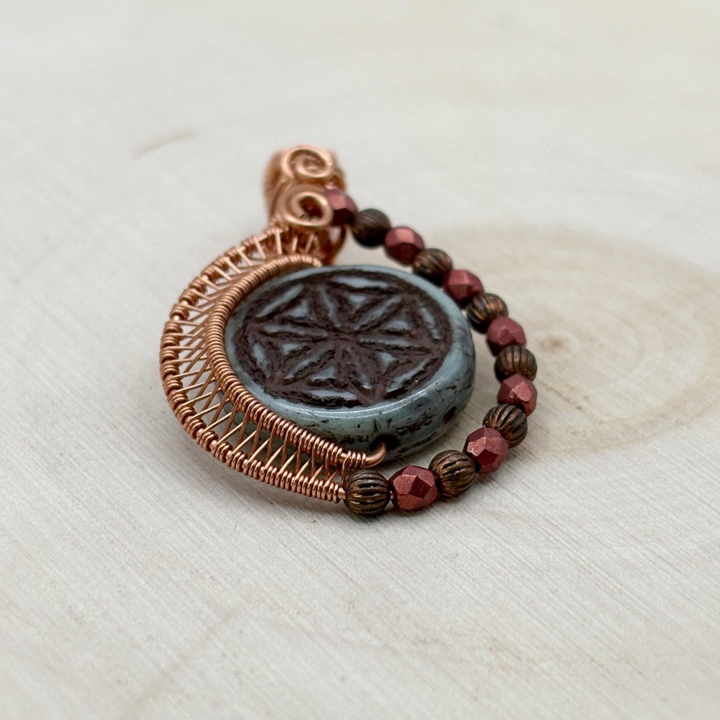 Glass pendant with copper wire wrapping and beads on a light wooden surface