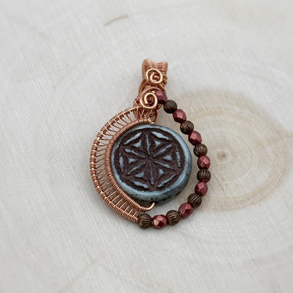 Pendant with copper wire wrapping and red beads on a light wooden surface