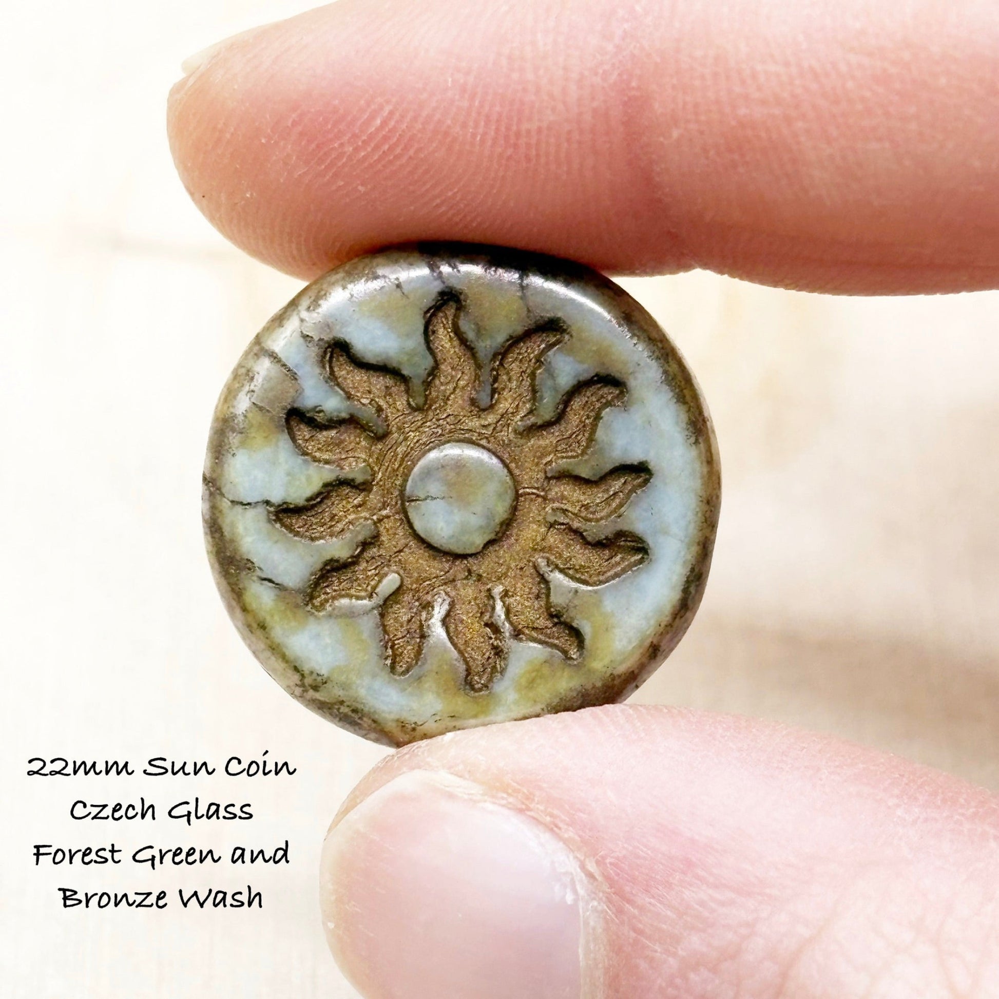 Glass sun coin with 'Forest Green and Bronze Wash' finish held between fingers.