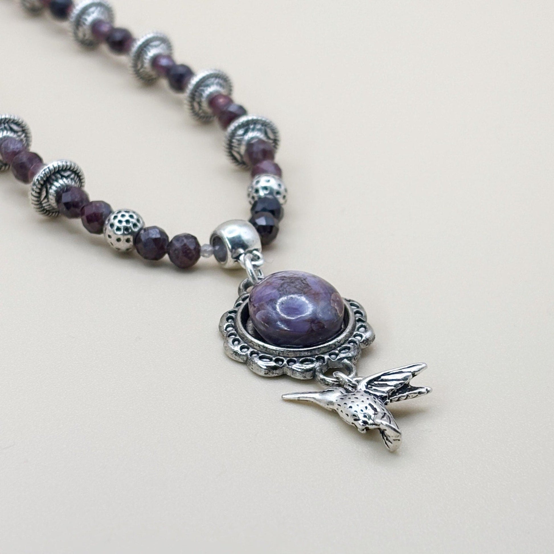 Necklace with purple beads and a silver bird charm on a light background