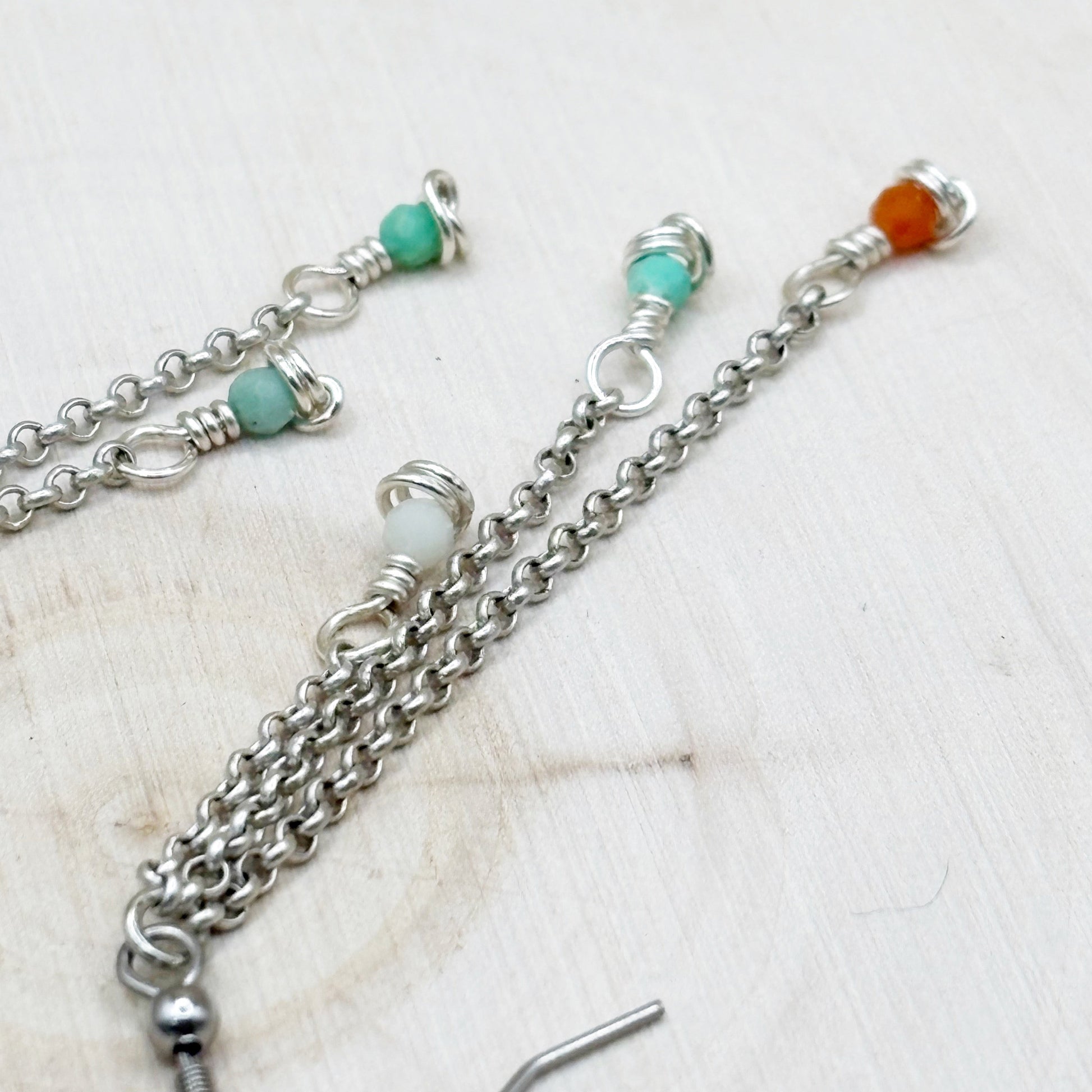 Silver chain necklace with turquoise and orange beads on a light wooden surface