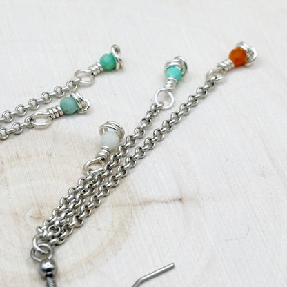Silver chain necklace with turquoise and orange beads on a light wooden surface
