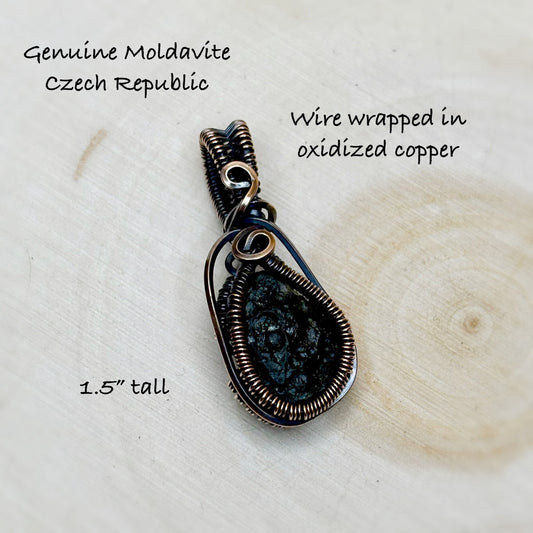 copper wire wrapped Moldavite tektite sitting on a wooden light background