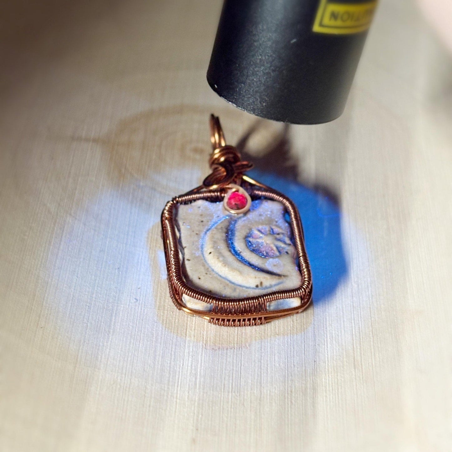 Jewelry pendant with a red gemstone being lit up with a black light on a white background
