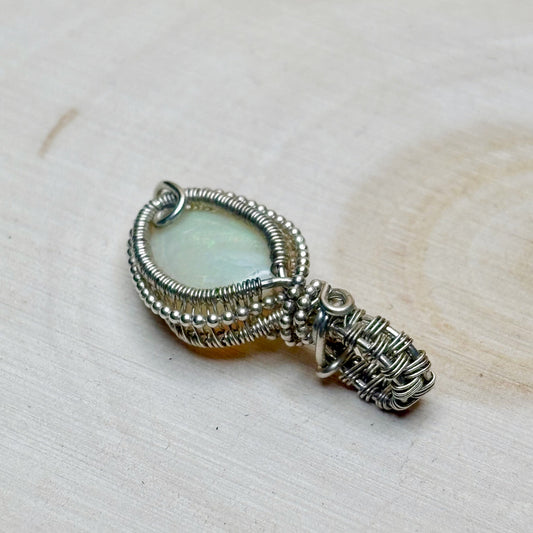 Silver wire-wrapped pendant with australian opal stone on a beige background