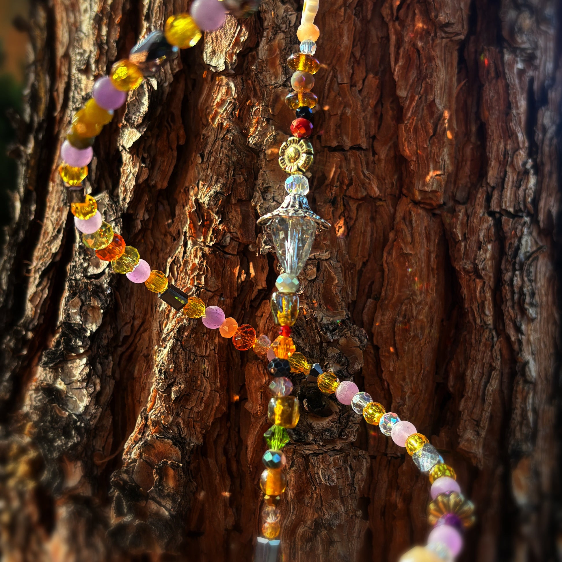 Colorful beaded decoration with a crystal pendant hanging on a tree trunk.