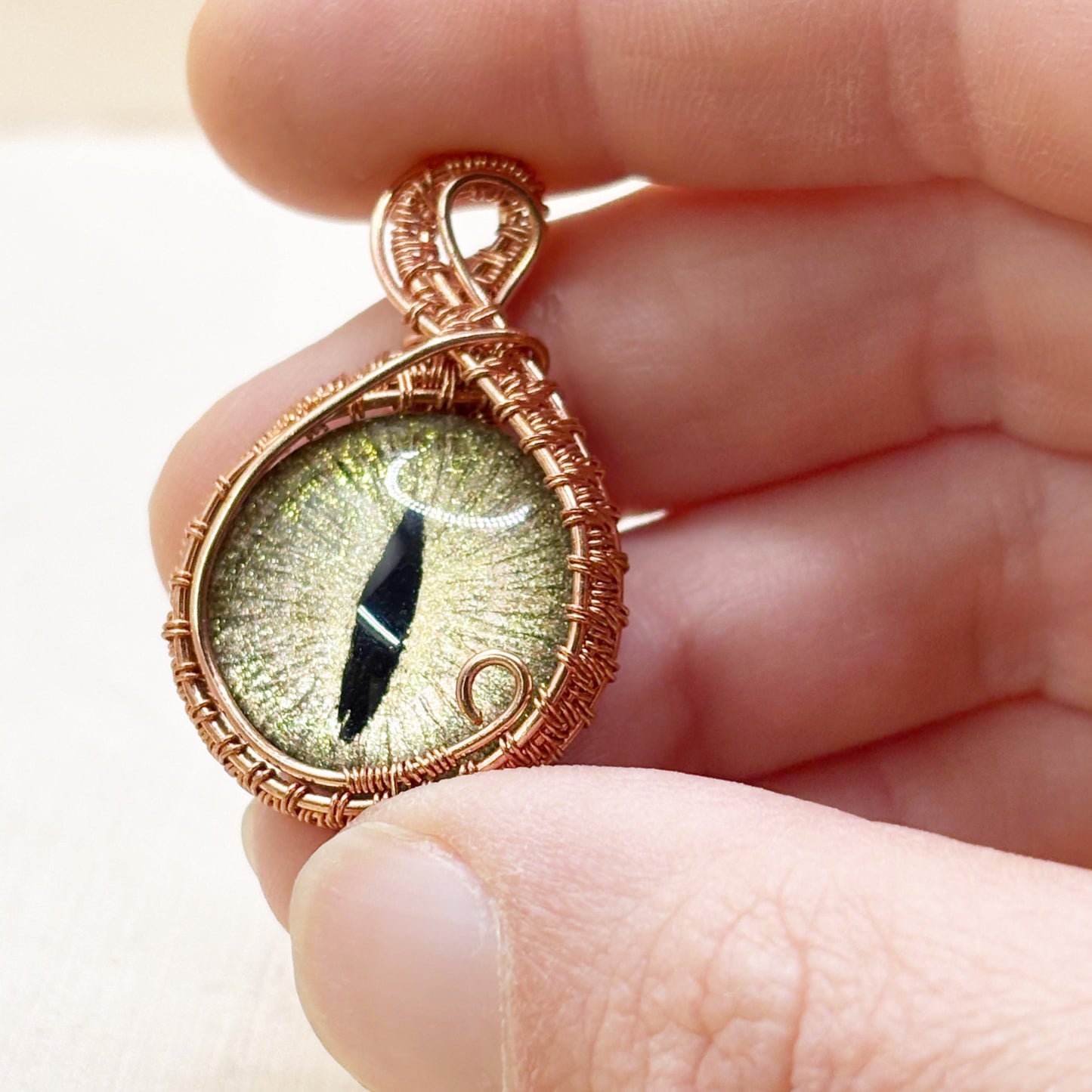 Hand holding a copper-wrapped pendant with a green eye design.