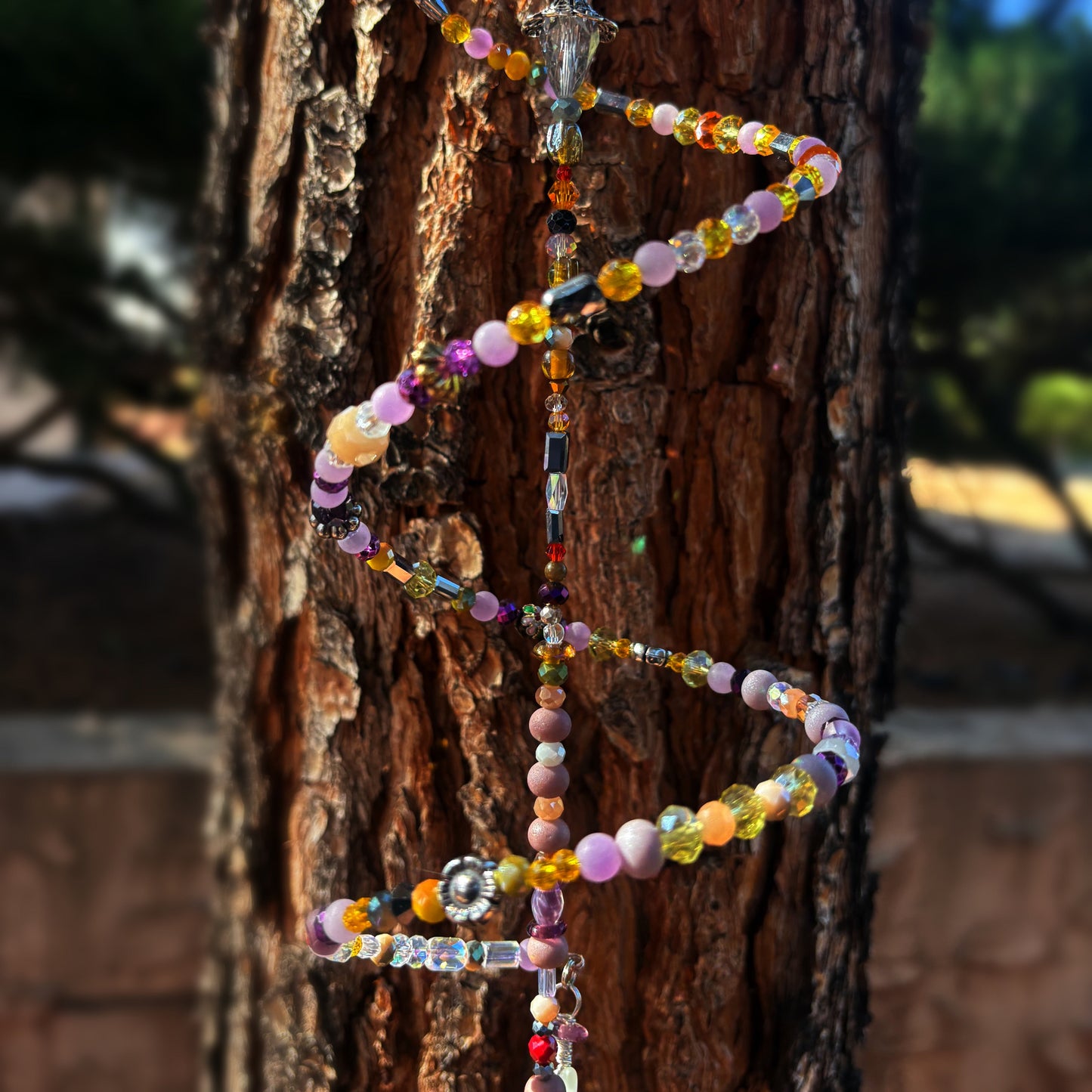 Colorful beaded sun catcher draped over a tree trunk with a blurred background
