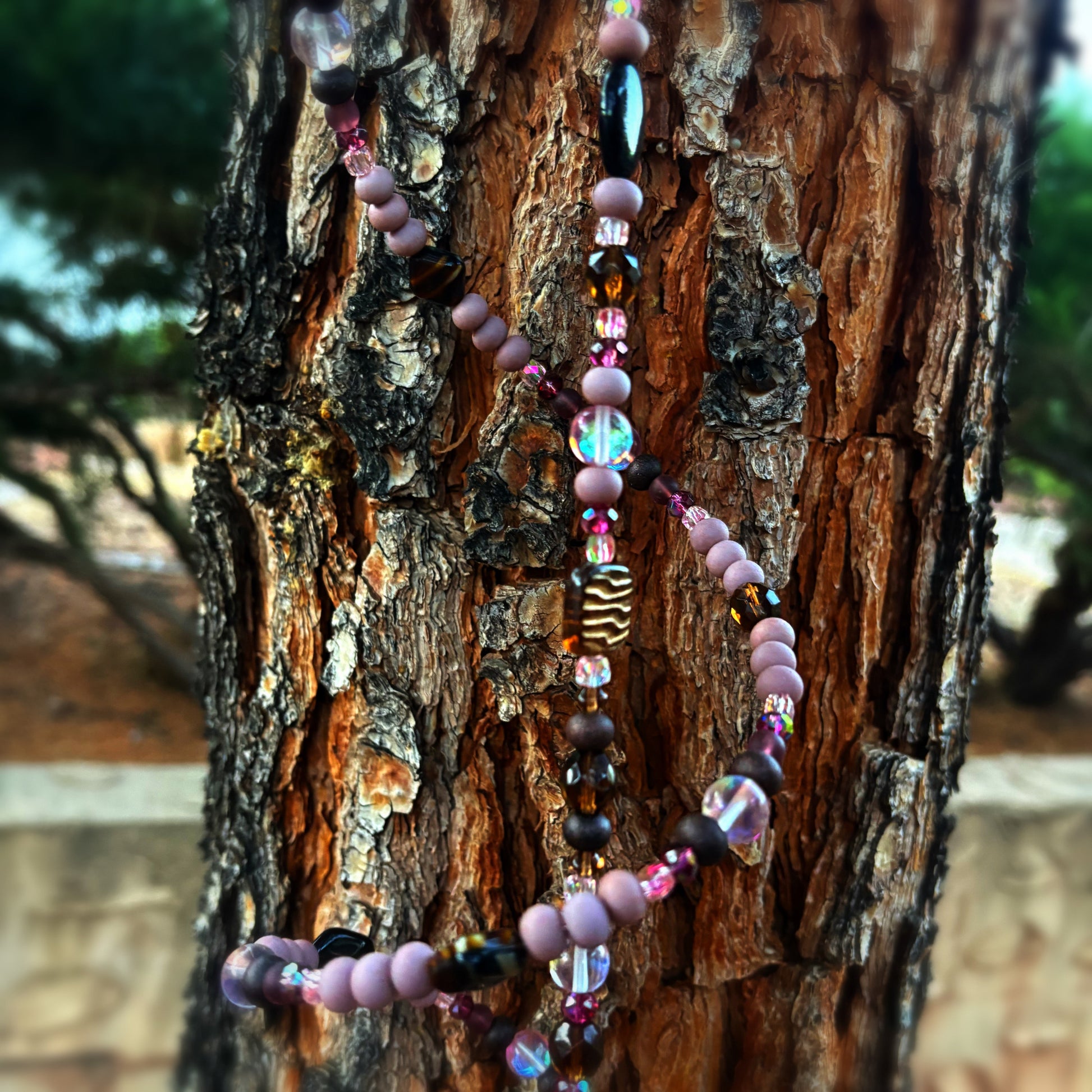 Colorful beaded art piece hanging on a tree trunk with a blurred natural background
