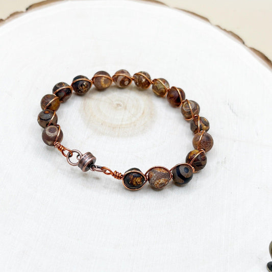 Brown beaded copper bracelet on a white wooden surface