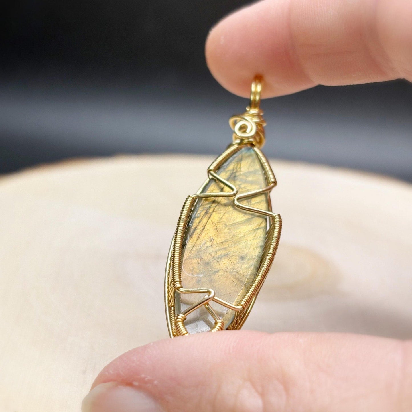 Gold-framed stone pendant held between fingers against a blurred background