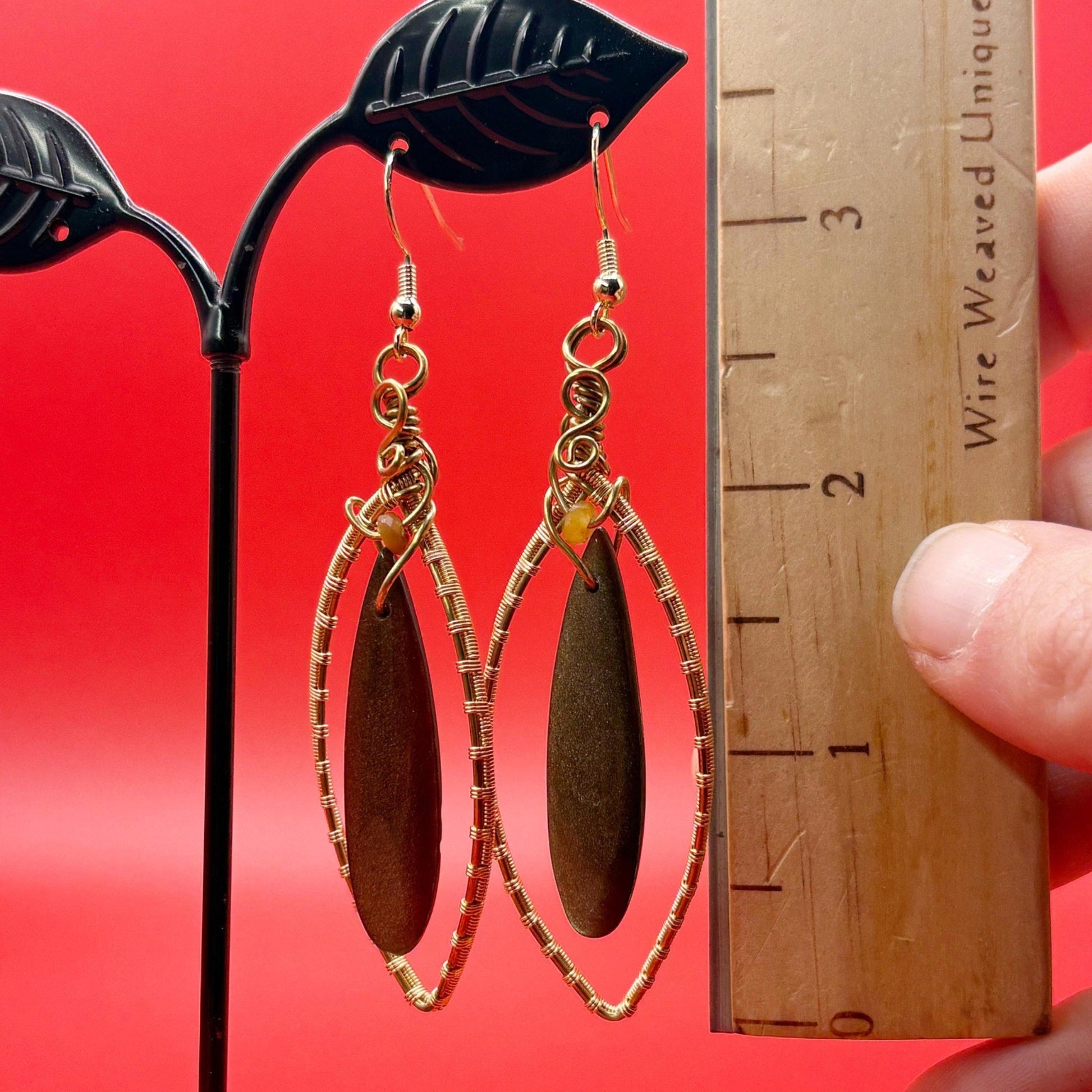obsidian with gold wire wrapping held against a red background with a wooden ruler for scale.