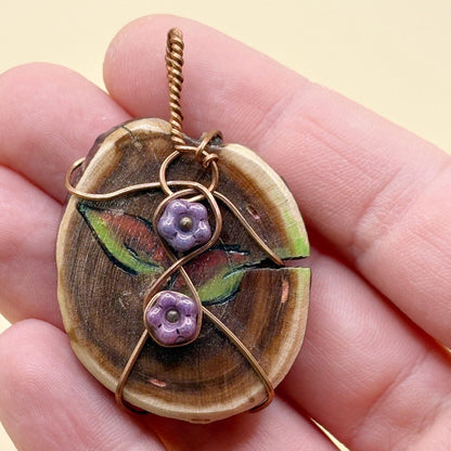 Wooden pendant with floral designs held in a hand against a beige background