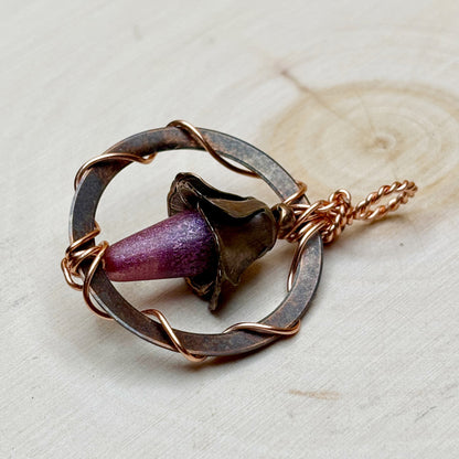 Necklace with a circular design and purple floral focal on a light background