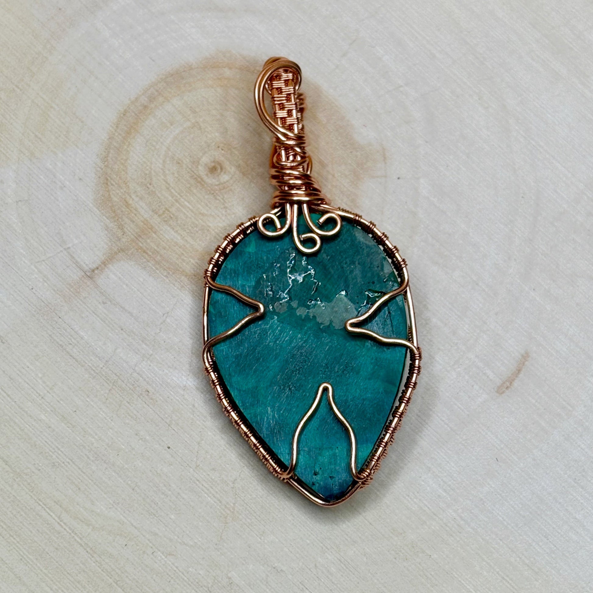 Malachite stone pendant with copper wire wrapping on a light wooden background