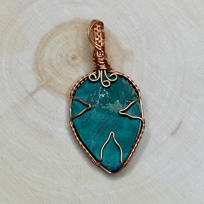 Malachite stone pendant with copper wire wrapping on a light wooden background