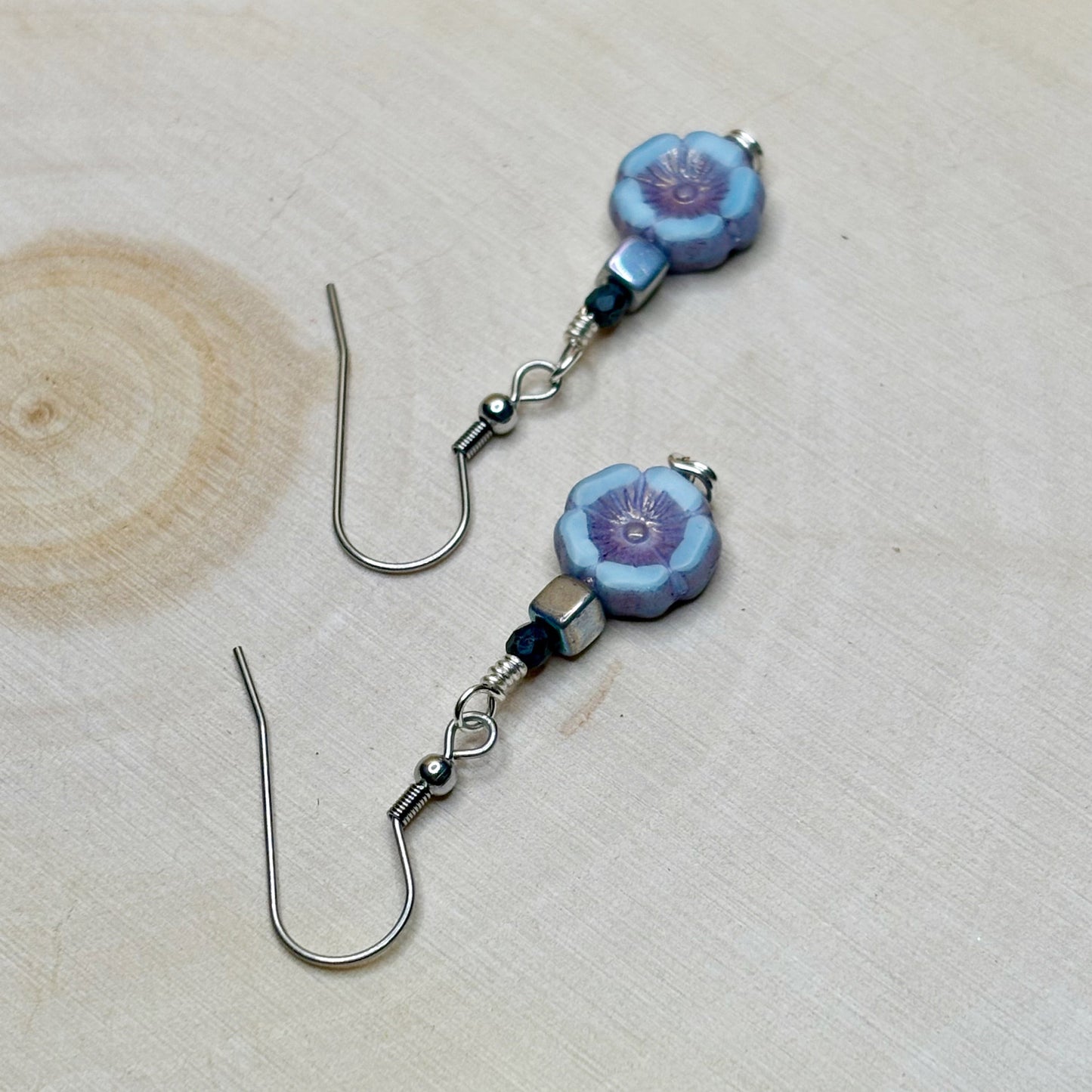 Pair of floral earrings with blue and purple flowers on a wooden surface