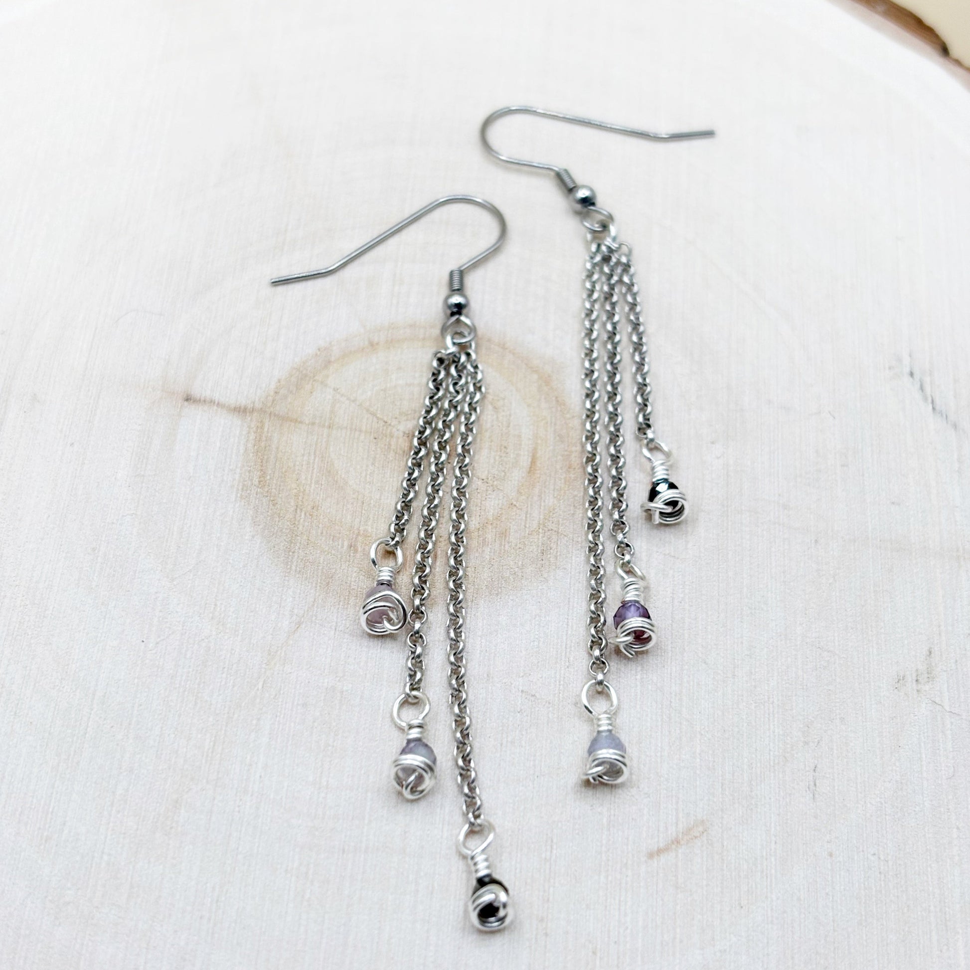 Silver chain earrings with small amethyst charms on a white fabric background