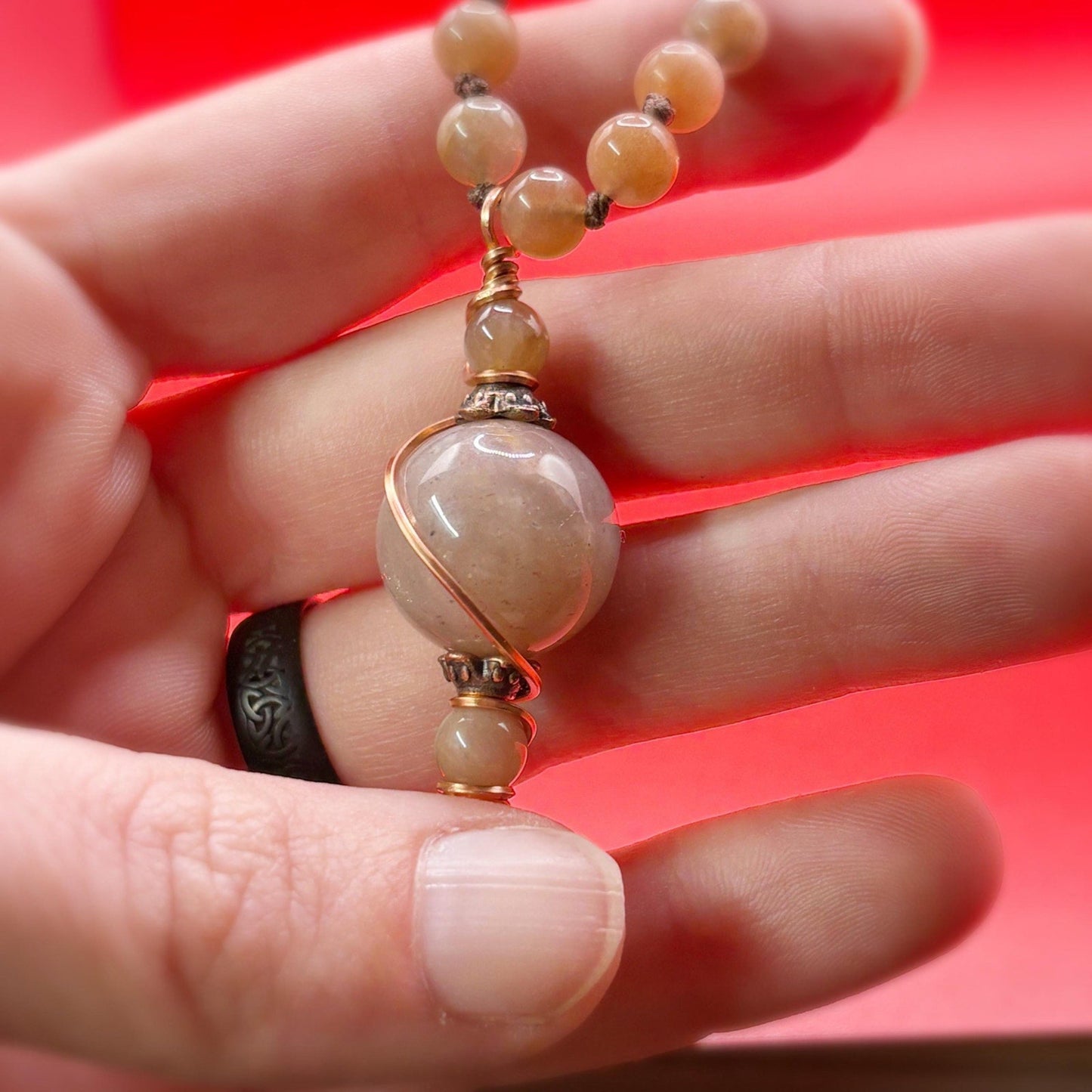 Close-up of a hand holding a beaded necklace against a red background