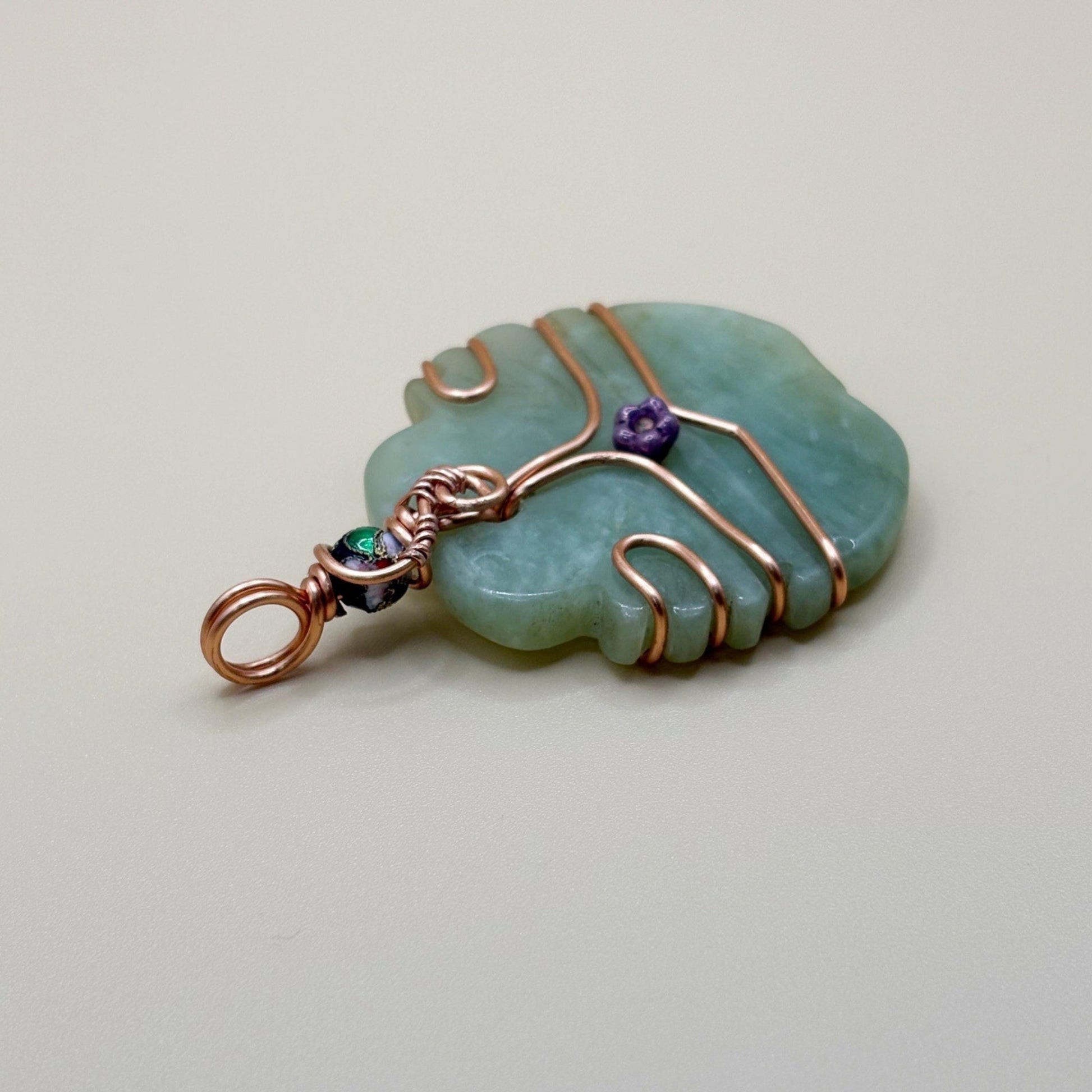 Jade pendant with copper wire wrapping on a light background