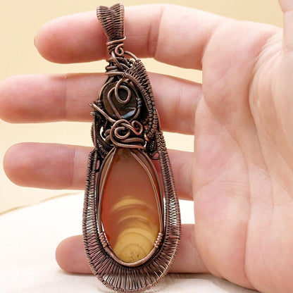 Hand holding a copper-wrapped pendant with a yellow and brown stone