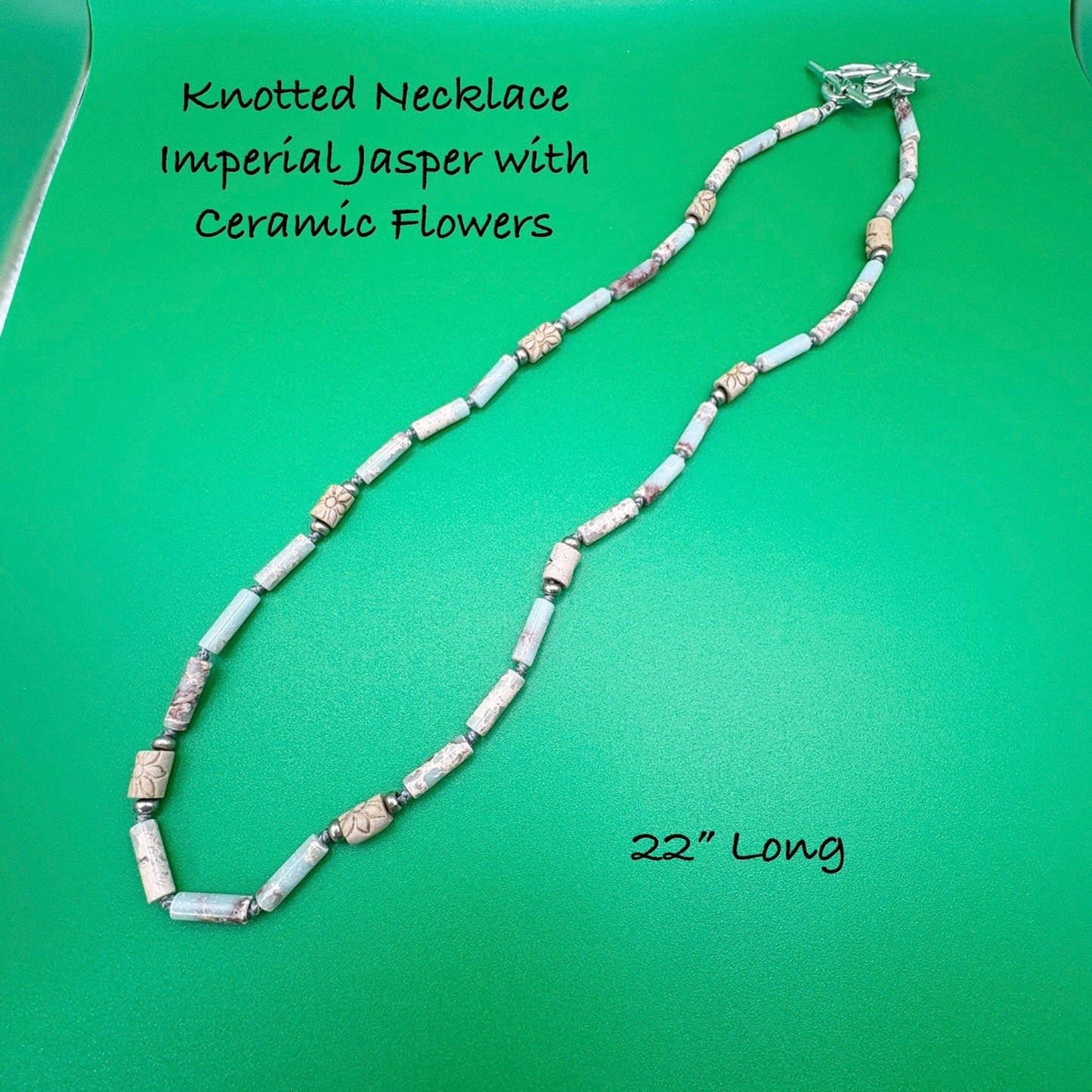 Knotted necklace with Imperial Jasper and ceramic flowers on a green background