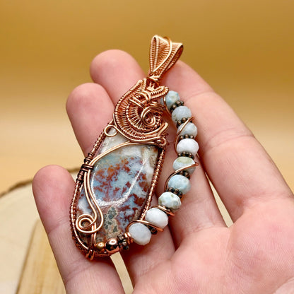 Hand holding a decorative pendant with a stone and beads against a blurred background