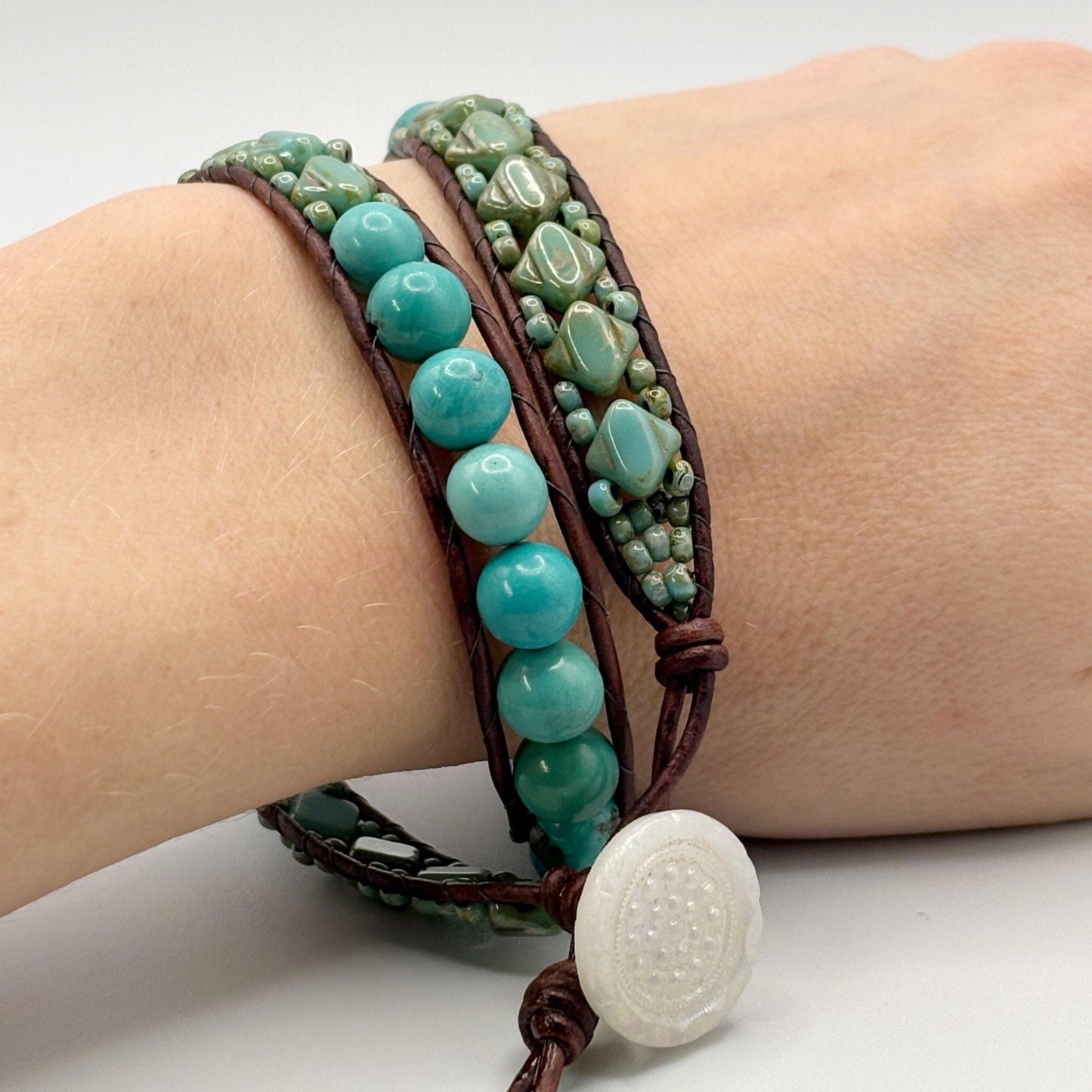 Turquoise beaded bracelet with brown leather strap on wrist against a white background