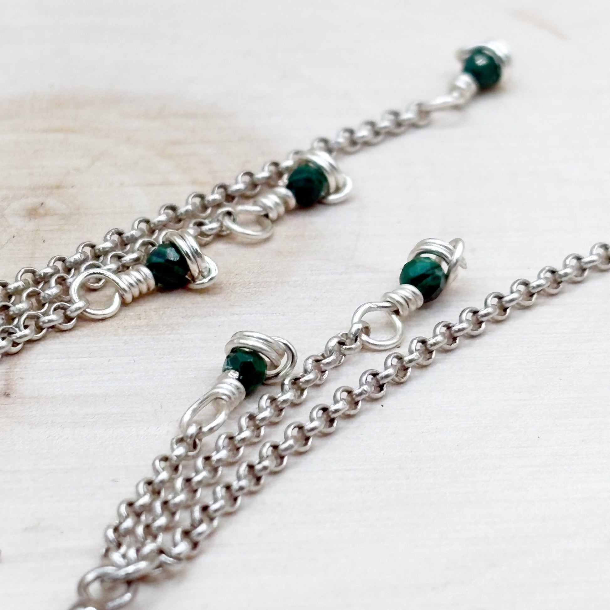 Silver chain with green beads on a light wooden surface