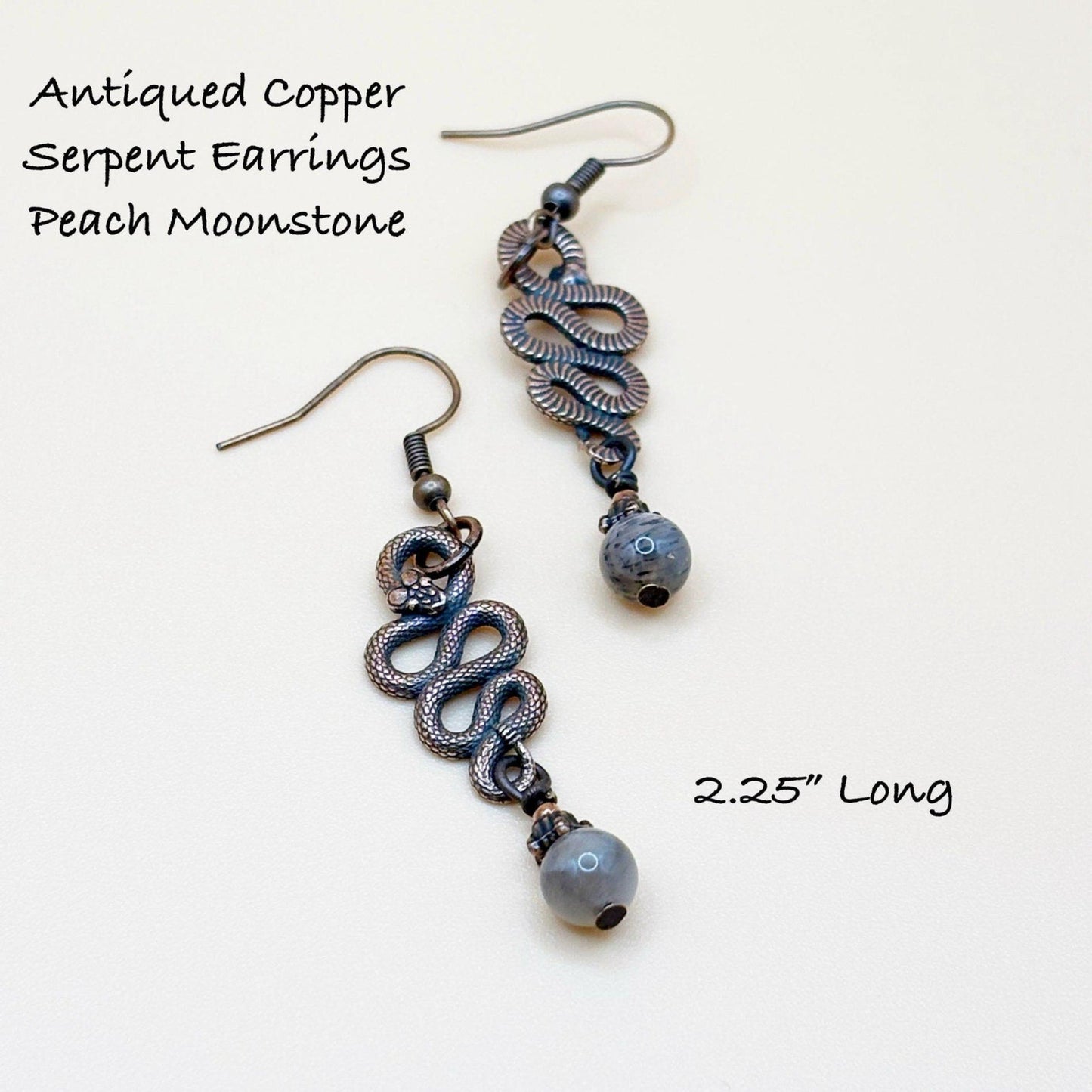Antiqued copper serpent earrings with peach moonstone beads on a white background