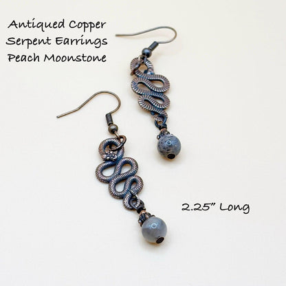 Antiqued copper serpent earrings with peach moonstone beads on a white background