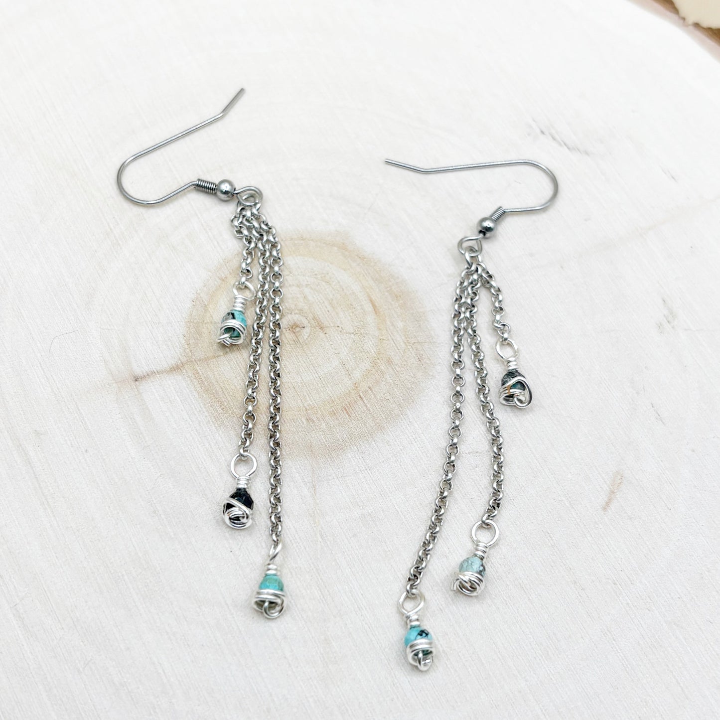 Silver chain earrings with turquoise charms on a wood background