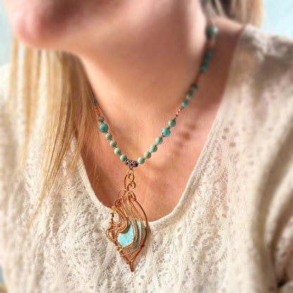 Turquoise beaded necklace with a decorative pendant worn by a person in a white lace top.
