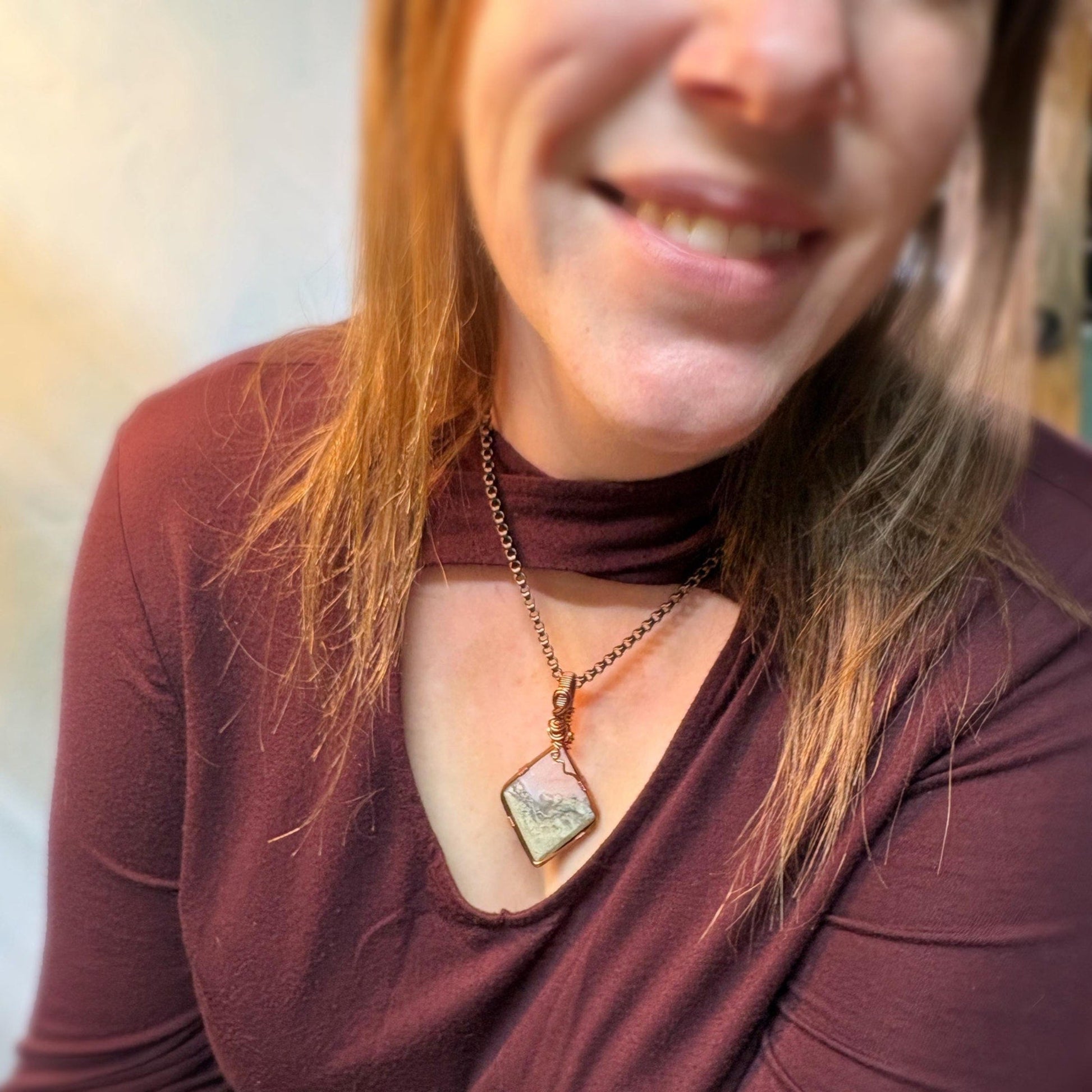 Woman wearing a maroon top with a necklace featuring a pendant.