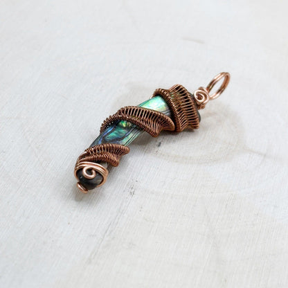 Copper-wrapped pendant with a central gemstone on a white wood background