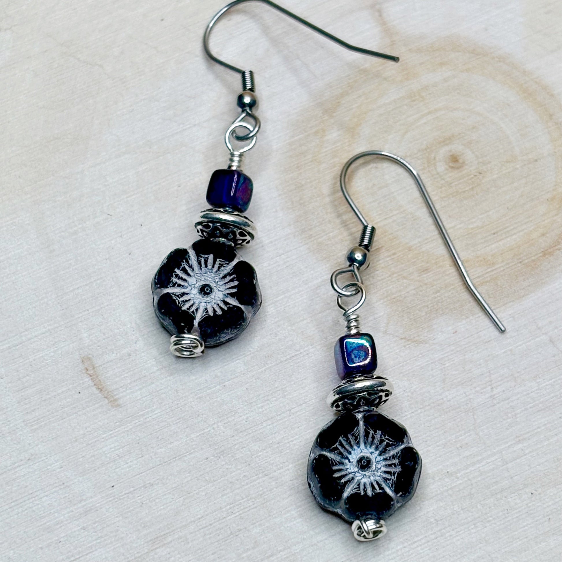 Pair of black beaded earrings with silver hooks on a light wooden surface