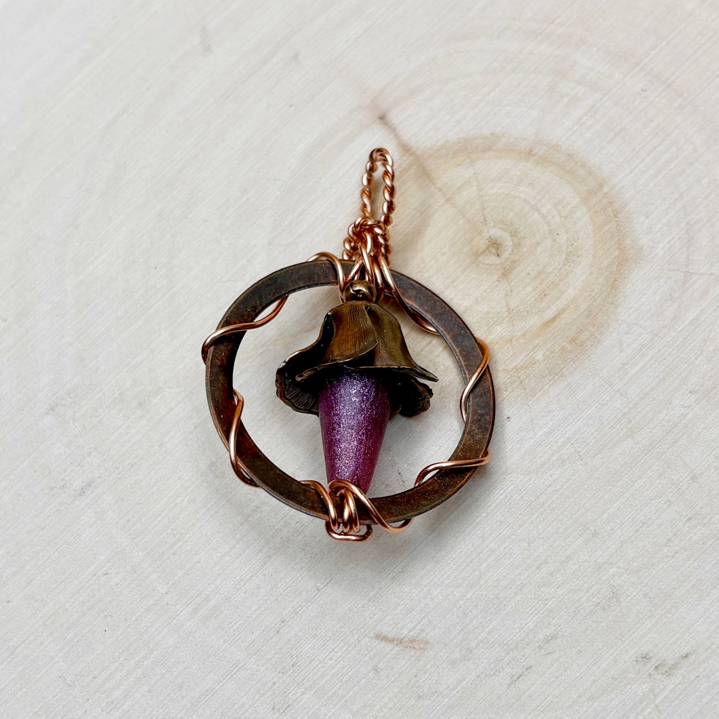 Jewelry pendant with a purple flower on a textured wooden background
